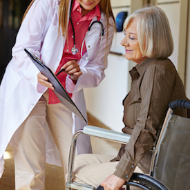Female Physician is talking to a female patient who is sitting in a wheelchair.
